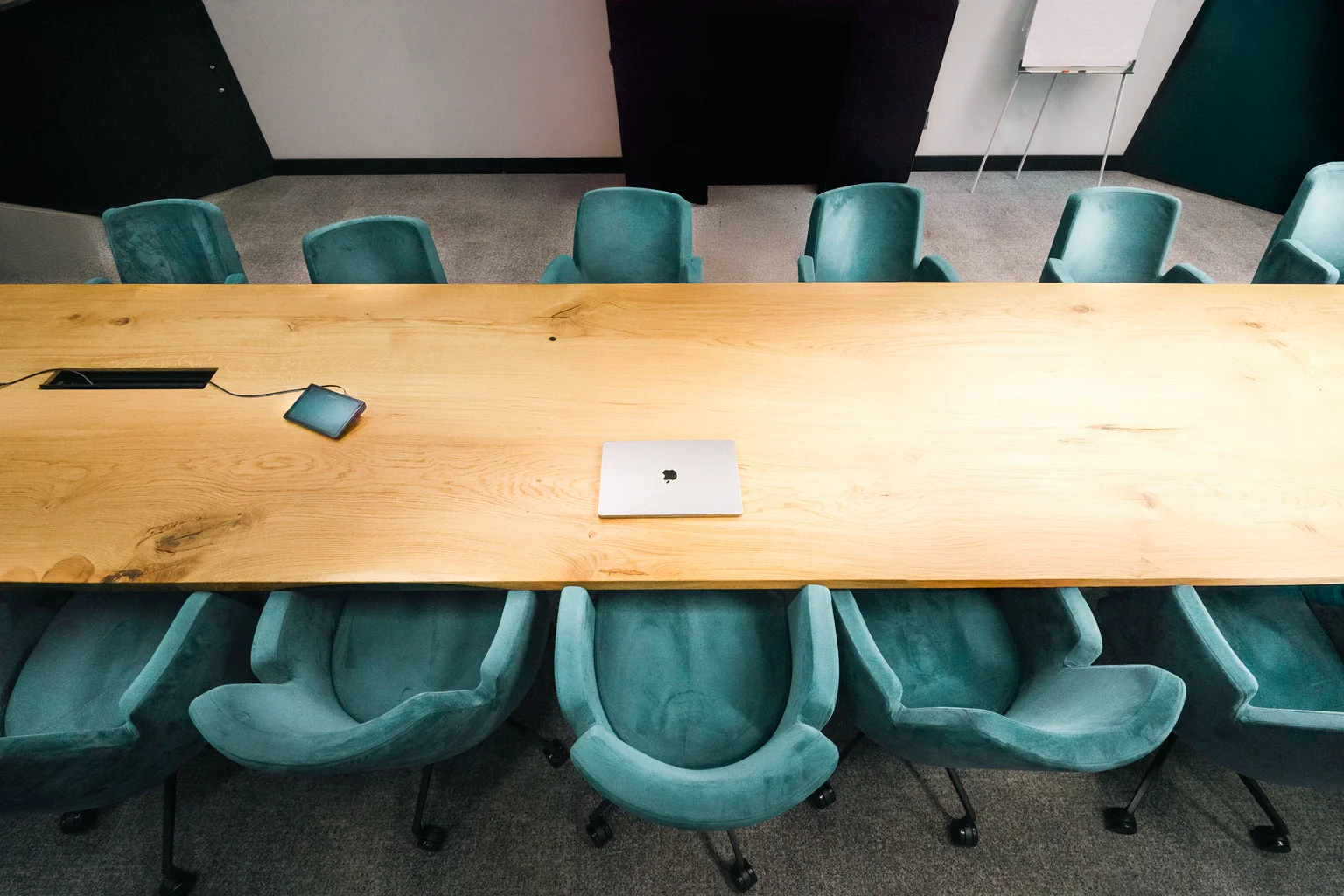 A wooden conference table with teal office chairs and a laptop.