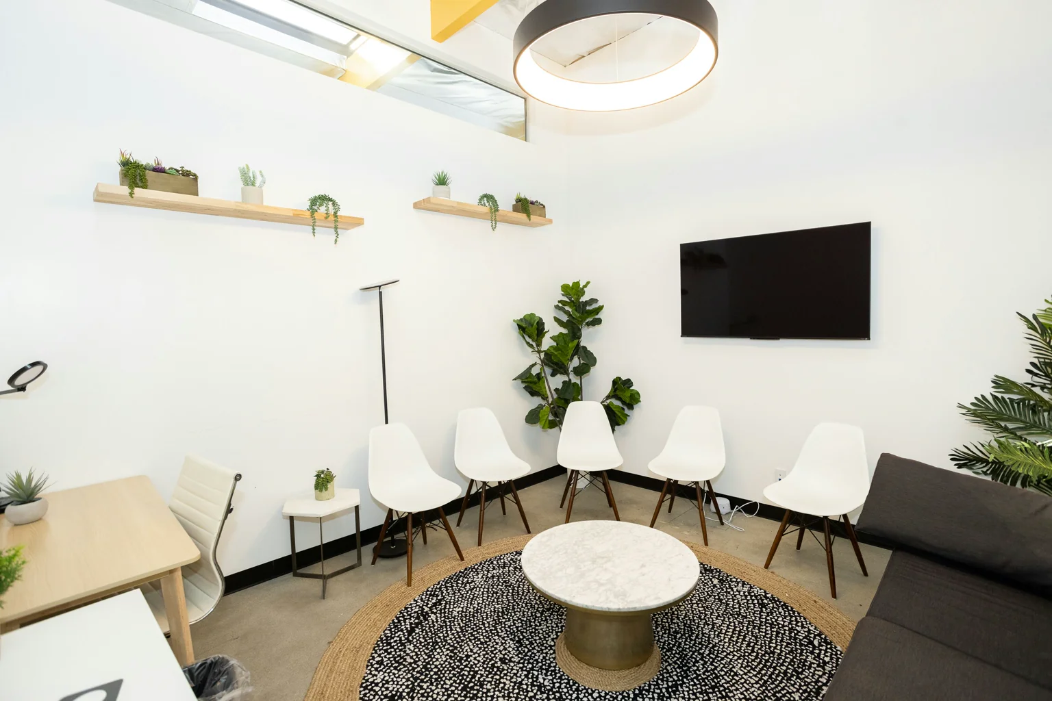 A bright waiting area with white chairs, plants and a small reception desk.